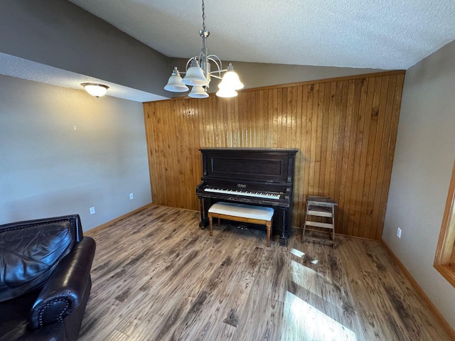 sitting room with a textured ceiling, a chandelier, vaulted ceiling, and wood finished floors