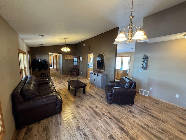 living room with a textured ceiling, a notable chandelier, wood finished floors, visible vents, and vaulted ceiling