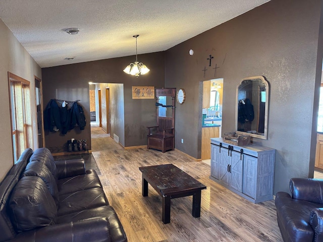 living room featuring light wood finished floors, visible vents, vaulted ceiling, and a textured ceiling