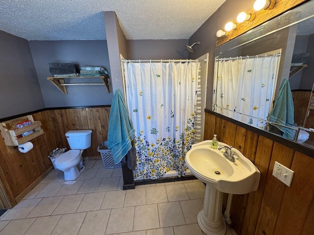 bathroom featuring curtained shower, toilet, wainscoting, wood walls, and a textured ceiling