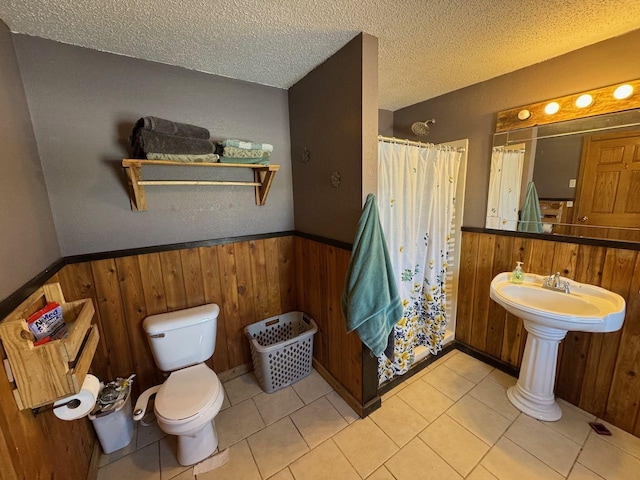 full bath with a textured ceiling, curtained shower, toilet, wooden walls, and a wainscoted wall