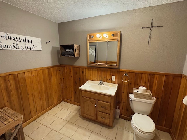 half bathroom with wainscoting, wood walls, a textured ceiling, and toilet