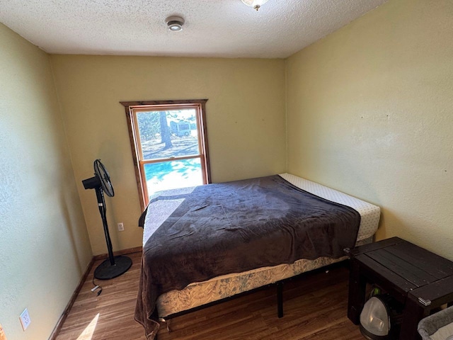 bedroom featuring a textured ceiling, baseboards, and wood finished floors