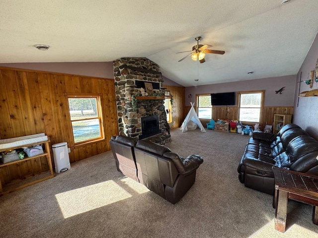 carpeted living area featuring wooden walls, a ceiling fan, vaulted ceiling, a textured ceiling, and a fireplace