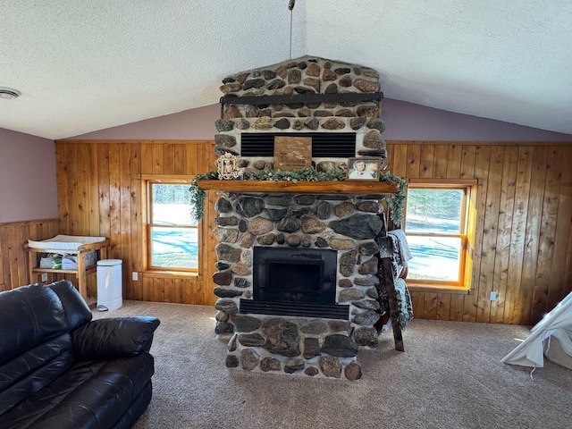 carpeted living room with a textured ceiling, a stone fireplace, wood walls, and lofted ceiling