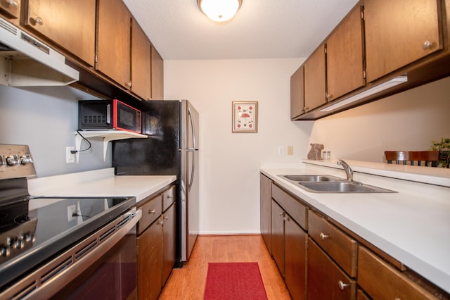 kitchen featuring under cabinet range hood, a sink, light wood-style floors, stainless steel range with electric cooktop, and light countertops