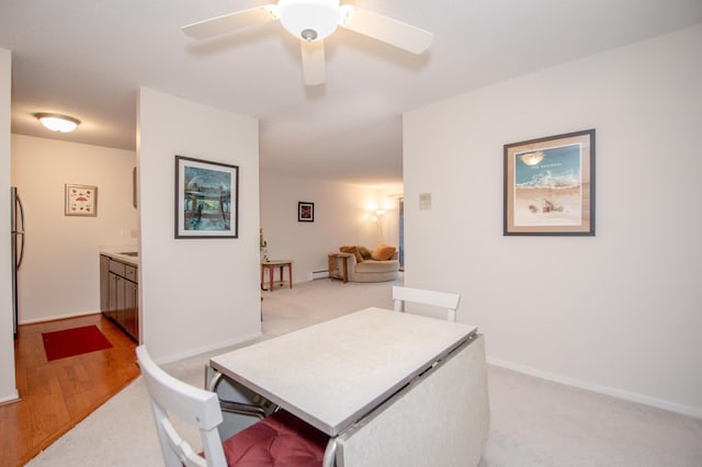 dining area with a ceiling fan, a baseboard radiator, light colored carpet, and baseboards