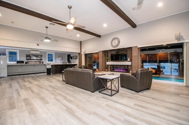 living area with a high ceiling, light wood-style floors, a large fireplace, ceiling fan, and beamed ceiling