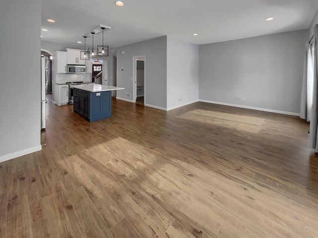 kitchen with recessed lighting, a kitchen island, wood finished floors, white cabinets, and appliances with stainless steel finishes