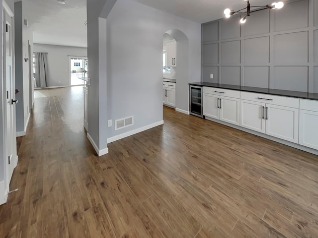 bar with arched walkways, visible vents, wood finished floors, beverage cooler, and baseboards