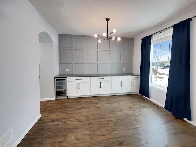 kitchen with beverage cooler, baseboards, dark countertops, dark wood-type flooring, and an inviting chandelier