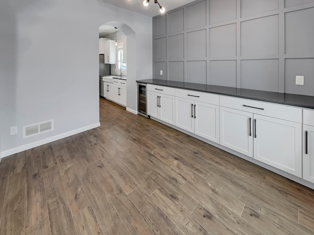 kitchen featuring arched walkways, dark countertops, visible vents, a decorative wall, and beverage cooler