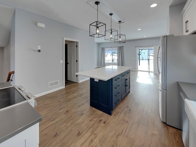 kitchen featuring a center island, visible vents, light wood-style floors, freestanding refrigerator, and white cabinetry