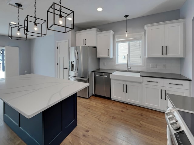 kitchen featuring a sink, light wood-style floors, appliances with stainless steel finishes, backsplash, and decorative light fixtures