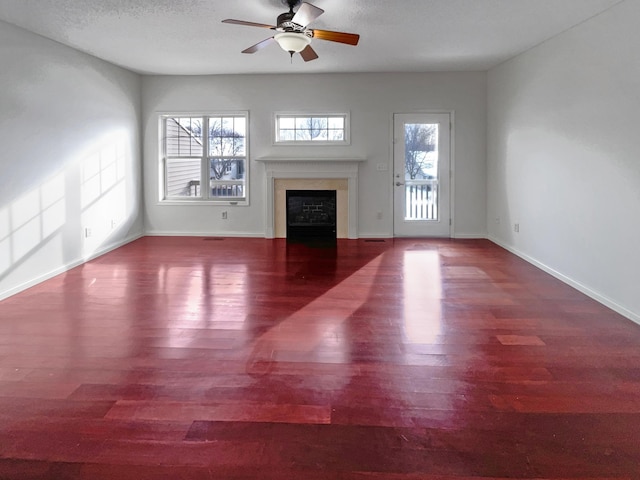 unfurnished living room featuring baseboards, ceiling fan, wood finished floors, a textured ceiling, and a fireplace