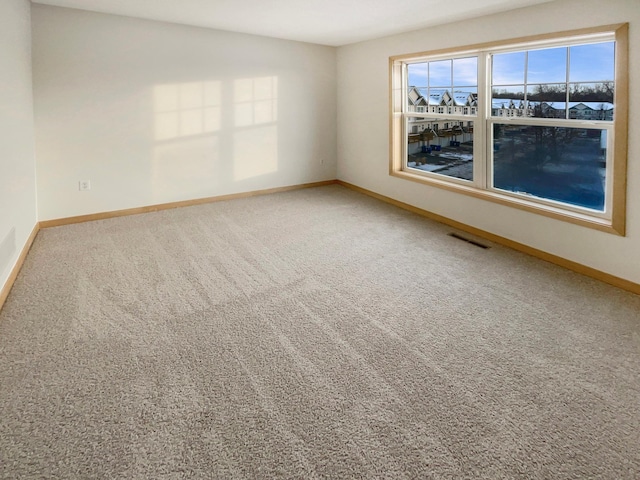 empty room with carpet floors, visible vents, and baseboards