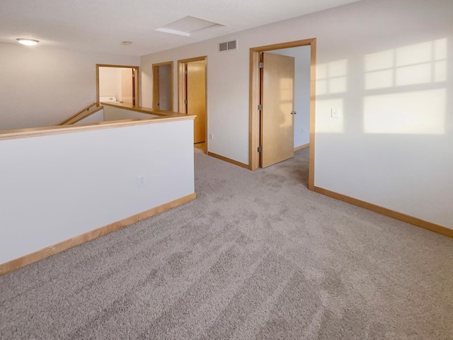 carpeted empty room with attic access, visible vents, and baseboards