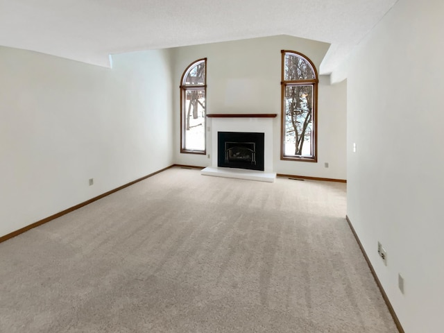 unfurnished living room featuring baseboards, a fireplace with raised hearth, a wealth of natural light, and carpet flooring