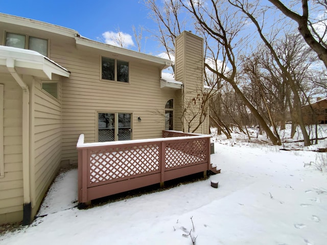 snow covered house with a chimney and a wooden deck