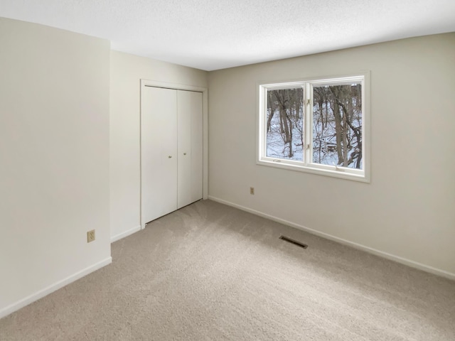 unfurnished bedroom with light carpet, baseboards, visible vents, a textured ceiling, and a closet