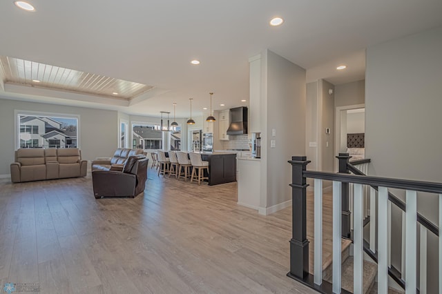 living area with baseboards, a tray ceiling, recessed lighting, and light wood-style floors