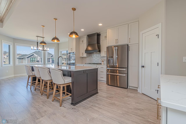 kitchen featuring light wood finished floors, backsplash, stainless steel appliances, premium range hood, and a sink