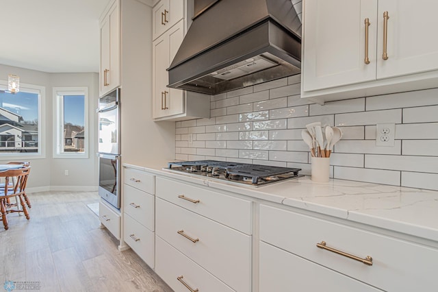 kitchen with light stone counters, stainless steel appliances, white cabinetry, tasteful backsplash, and custom range hood