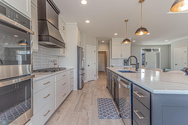 kitchen featuring light wood-style flooring, appliances with stainless steel finishes, premium range hood, white cabinetry, and a sink