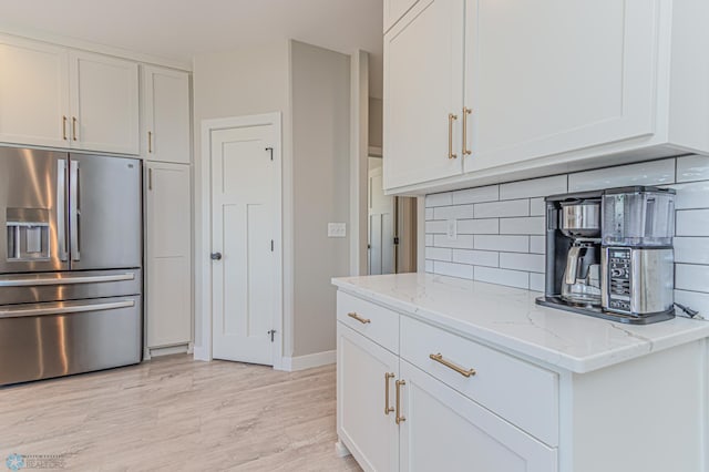 kitchen with light wood finished floors, tasteful backsplash, stainless steel fridge with ice dispenser, light stone countertops, and white cabinetry