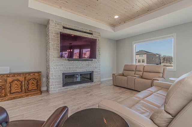 living room with wood ceiling, a raised ceiling, wood finished floors, and a stone fireplace