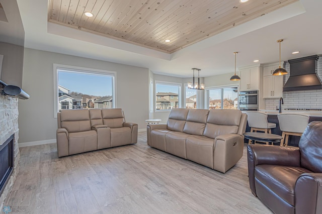 living area featuring light wood finished floors, baseboards, wood ceiling, a tray ceiling, and a stone fireplace