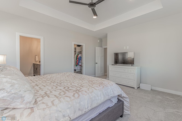 bedroom with a tray ceiling, a closet, a spacious closet, light carpet, and baseboards