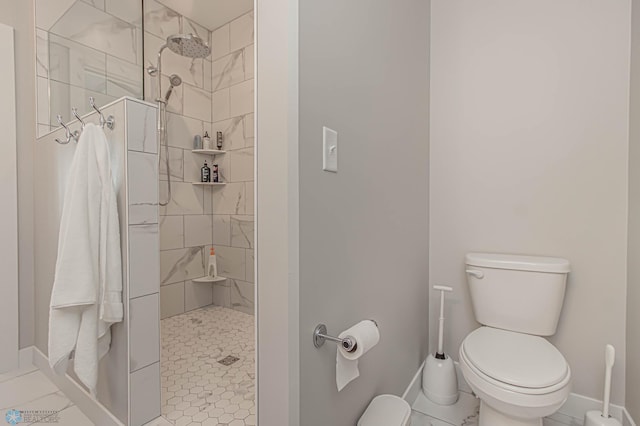 bathroom with tiled shower, toilet, and baseboards