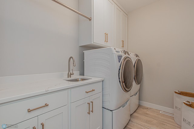 washroom featuring washing machine and clothes dryer, cabinet space, a sink, light wood-type flooring, and baseboards