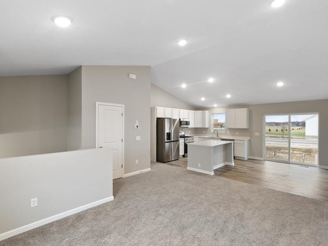 kitchen featuring stainless steel appliances, open floor plan, white cabinets, a sink, and a kitchen island