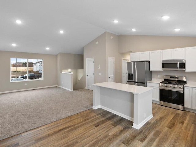 kitchen with wood finished floors, vaulted ceiling, stainless steel appliances, light countertops, and white cabinetry