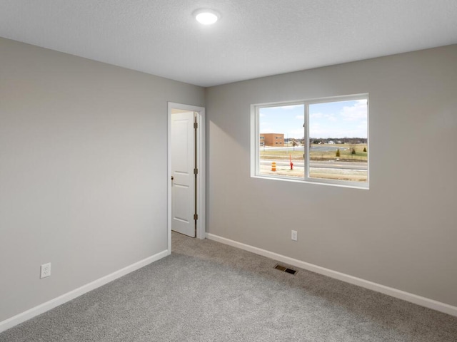 empty room with a textured ceiling, carpet flooring, visible vents, and baseboards