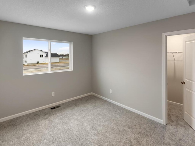 empty room featuring baseboards, visible vents, a textured ceiling, and carpet flooring