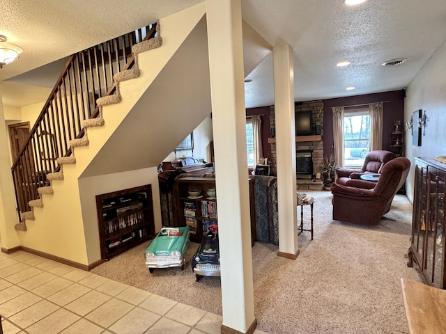 carpeted living room featuring visible vents, baseboards, tile patterned flooring, a textured ceiling, and a stone fireplace