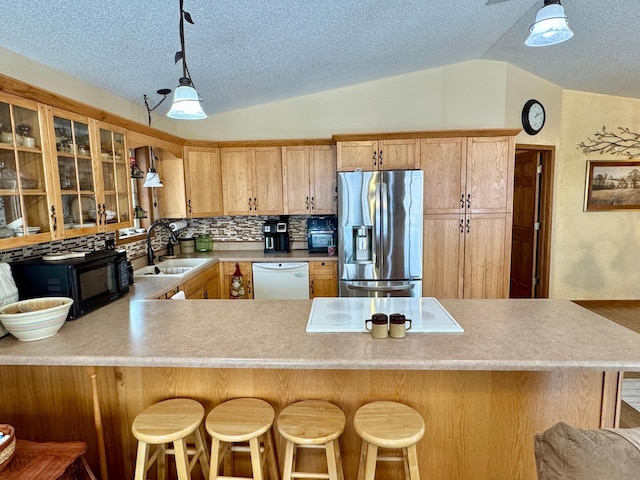 kitchen featuring white appliances, a sink, vaulted ceiling, backsplash, and glass insert cabinets