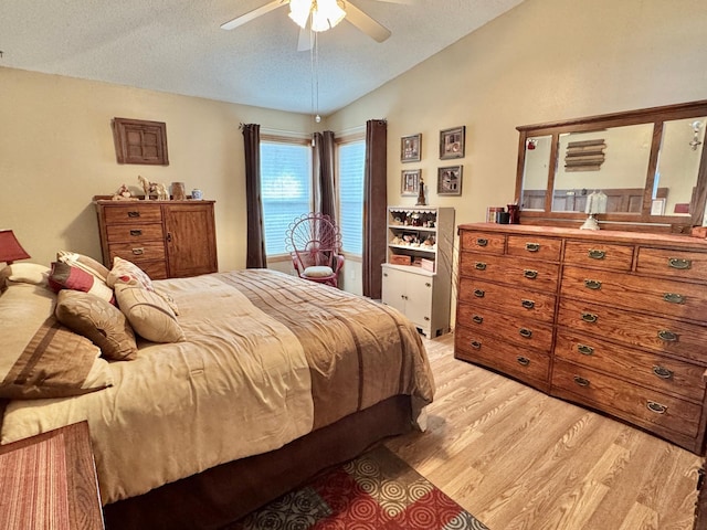 bedroom with light wood-style floors, vaulted ceiling, a textured ceiling, and ceiling fan