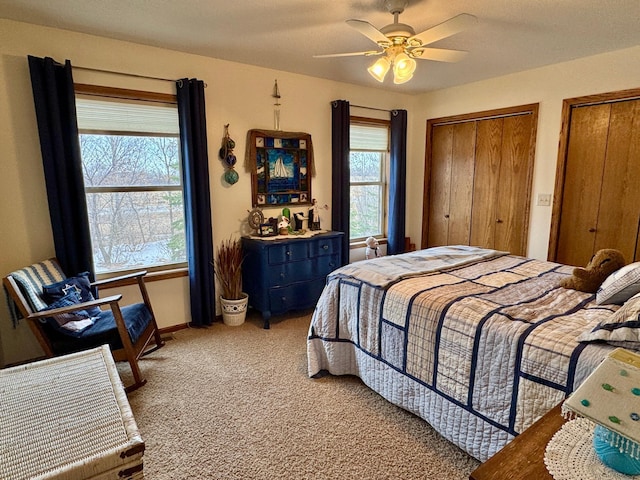 bedroom with multiple closets, a ceiling fan, light carpet, and multiple windows