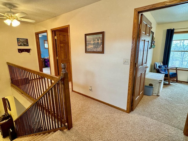 hallway with carpet, baseboards, a textured ceiling, and an upstairs landing