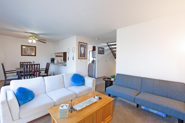 carpeted living room featuring ceiling fan and stairway