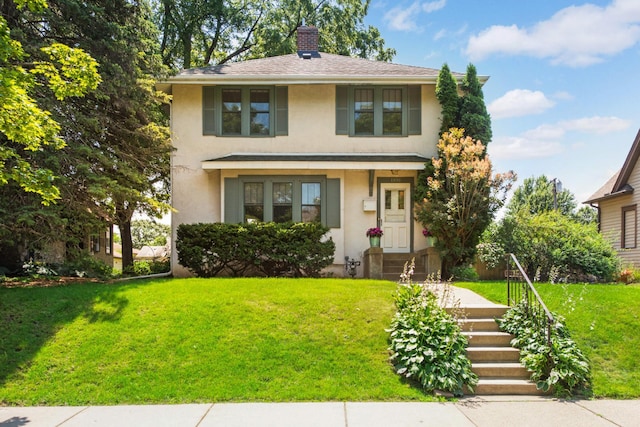 american foursquare style home featuring a shingled roof, a front yard, a chimney, and stucco siding