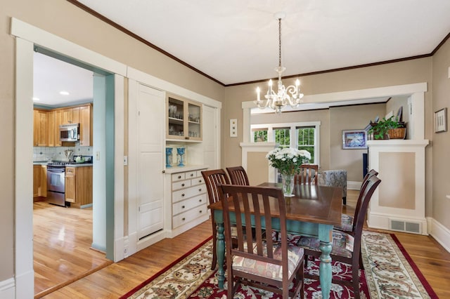 dining room with a chandelier, visible vents, crown molding, and light wood-style flooring