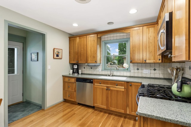 kitchen with stainless steel appliances, light wood-type flooring, brown cabinetry, and a sink