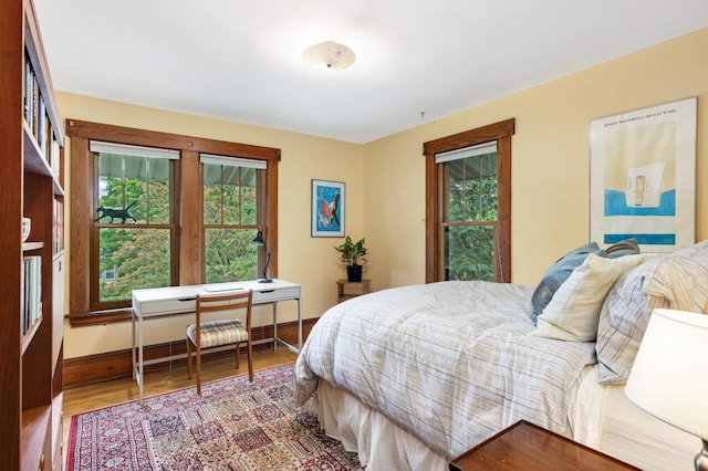 bedroom with multiple windows, wood finished floors, and baseboards