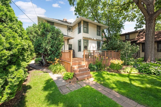 rear view of house with a yard, a wooden deck, a chimney, and stucco siding