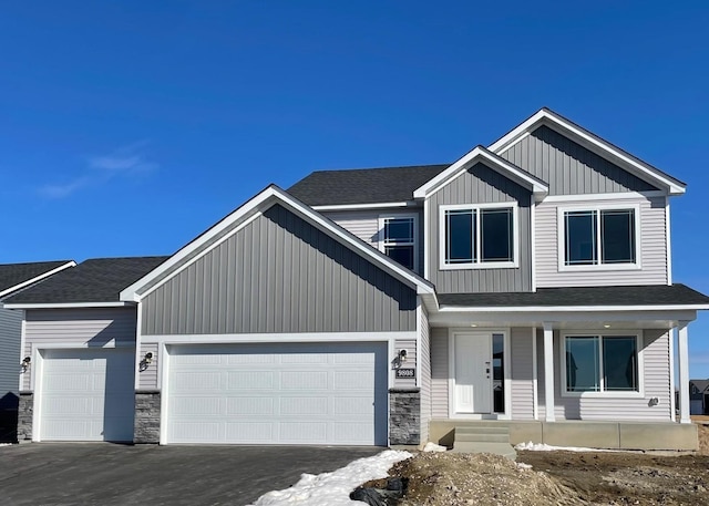 view of front of home featuring an attached garage, stone siding, a shingled roof, and board and batten siding